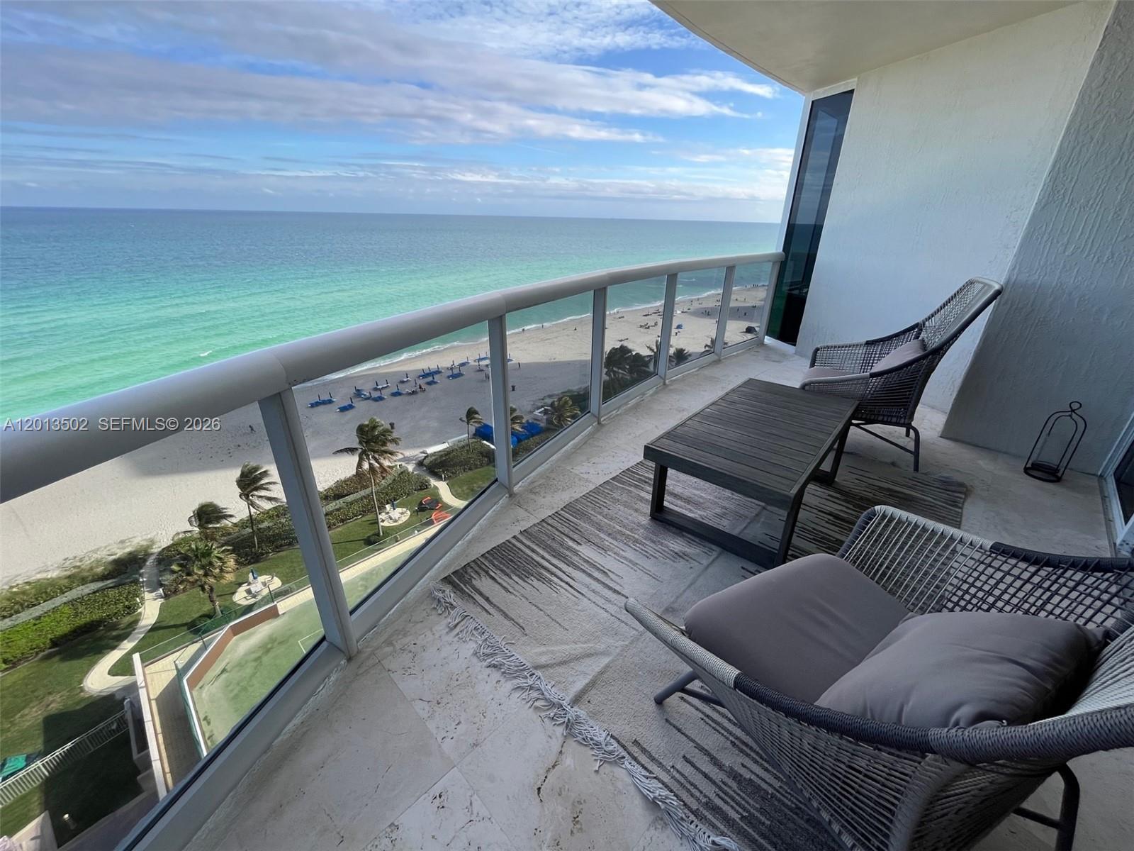 A balcony with outdoor furniture overlooks a sandy beach and the ocean — SUNNY ISLES BEACH, FL