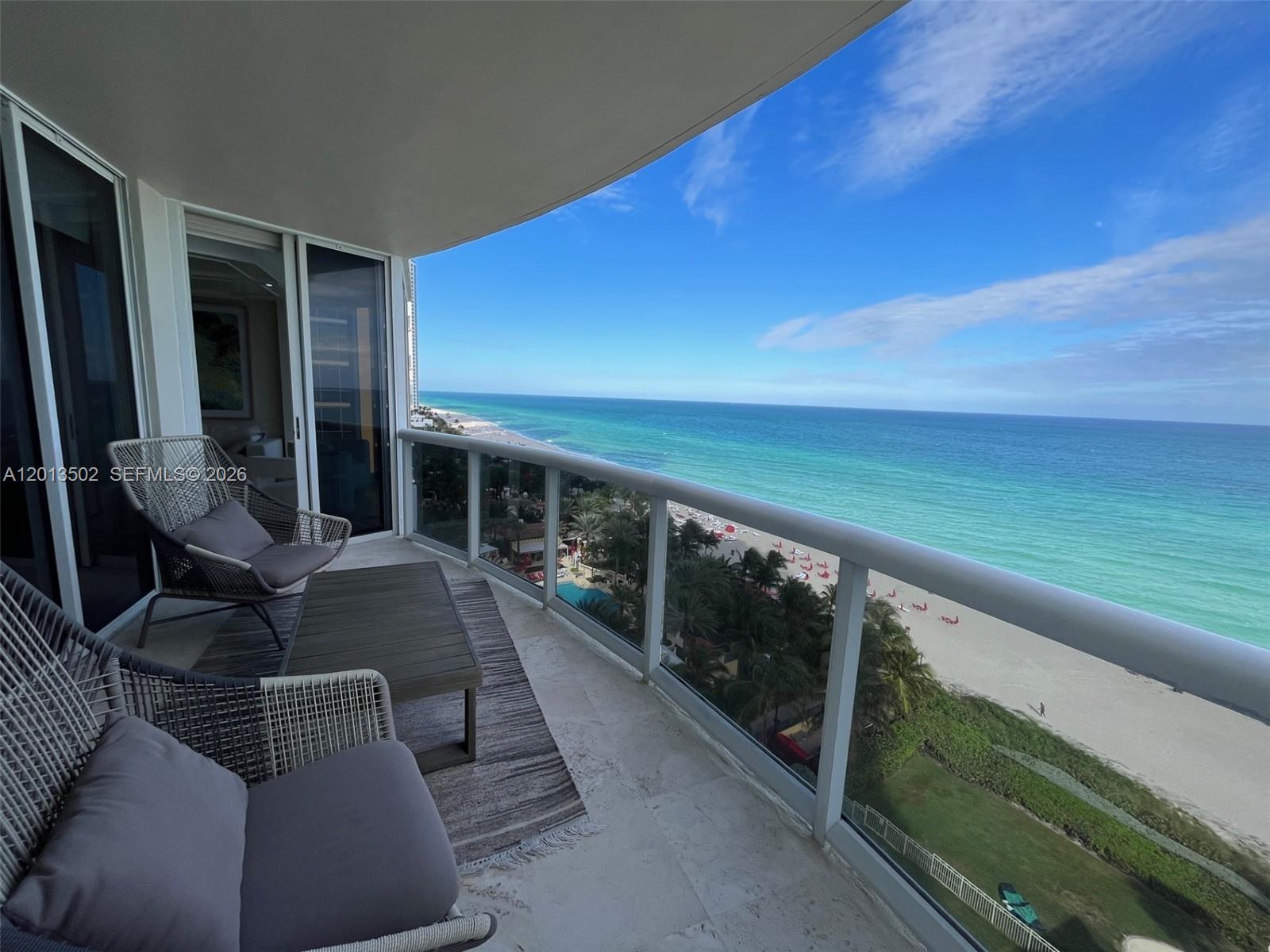 A balcony with outdoor furniture overlooks a sandy beach and the turquoise ocean — SUNNY ISLES BEACH, FL