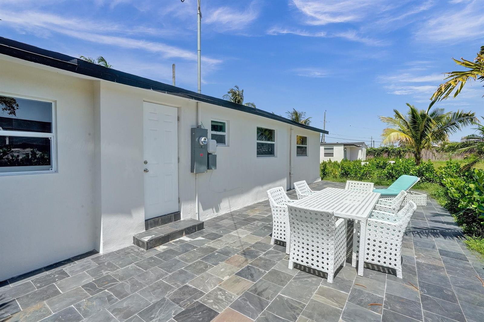 A white exterior wall with a door and patio furniture on a stone-tiled patio — 8021 NW 1st Place # 1, Miami FL 33150, MIAMI, FL