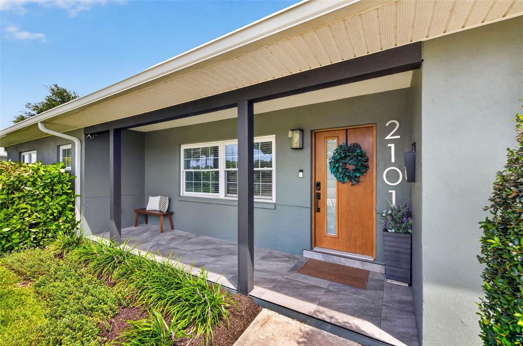A covered front porch features a wooden door, tiled flooring, and a small wooden bench — 2101 37TH STREET N, ST PETERSBURG, FL