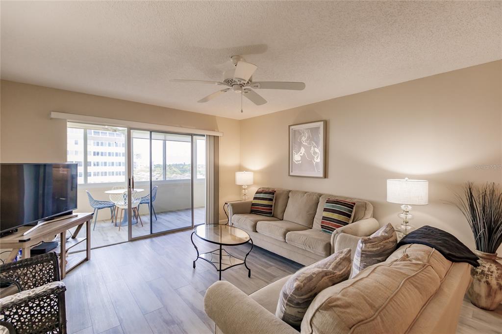A living room features light wood-look flooring, a beige sofa, and a sliding glass door — 1055 W PEPPERTREE DRIVE UNIT 506AA, SARASOTA, FL