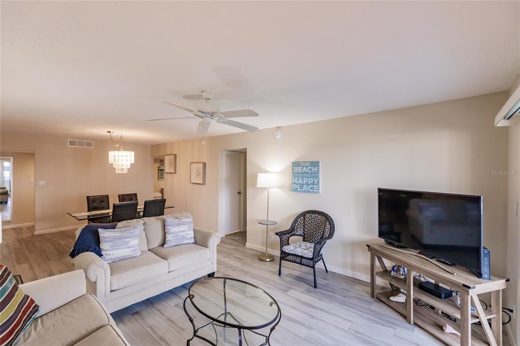 A living room with light wood-look flooring, a beige sofa, and a television on a stand — 1055 W PEPPERTREE DRIVE UNIT 506AA, SARASOTA, FL