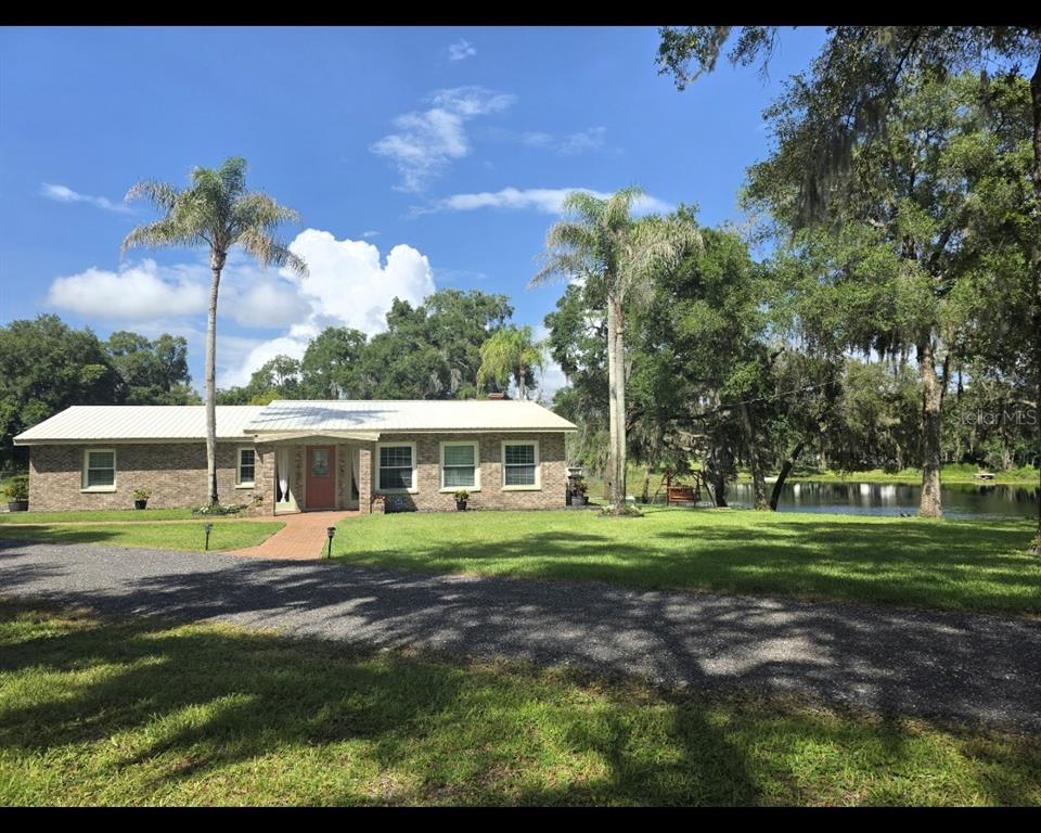 A single-story brick house with a metal roof sits on a grassy lot near water — 210 WESTLAKE DRIVE, LAKE HELEN, FL