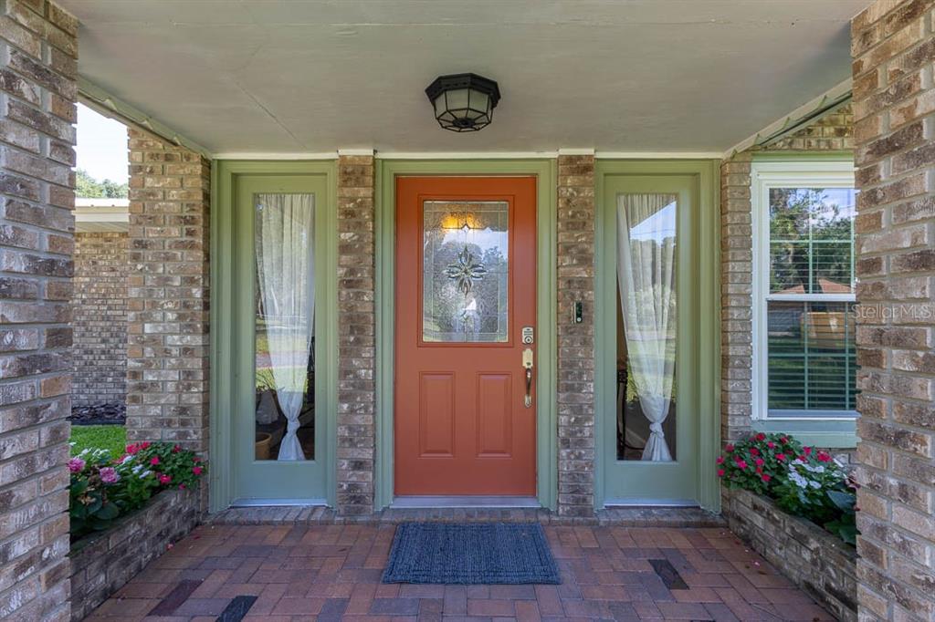 A brick-paved porch features a central orange front door flanked by two green sidelights — 210 WESTLAKE DRIVE, LAKE HELEN, FL