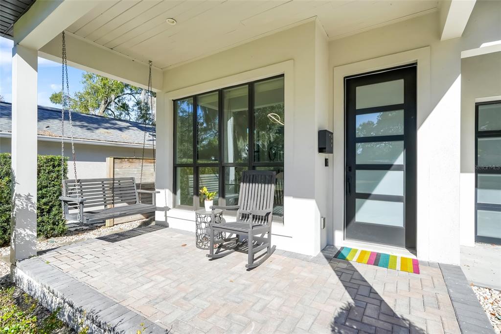 A covered front porch features a hanging bench, a rocking chair, and a modern front door — 1751 GOODRICH AVENUE, WINTER PARK, FL