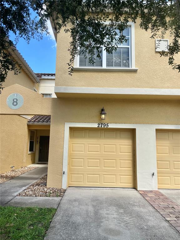 A two-story yellow stucco townhouse features a garage and a covered entryway — 2795 OAKWATER DR, KISSIMMEE, FL