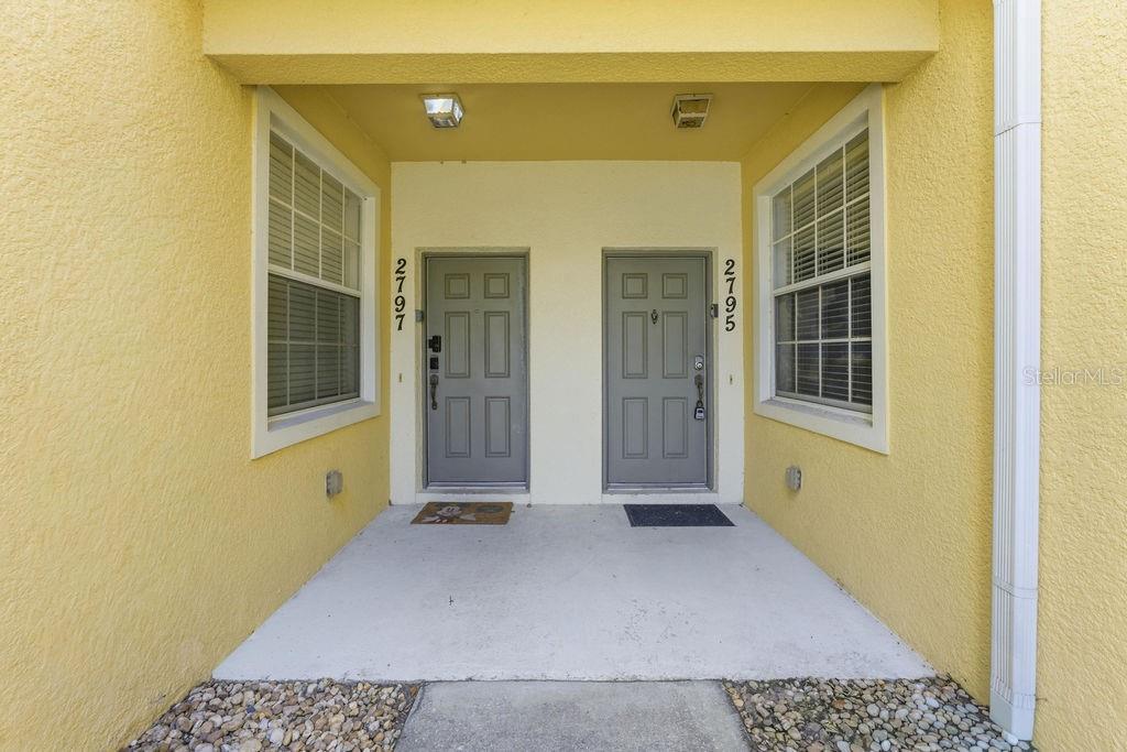 A covered entryway features two gray front doors with house numbers on a yellow wall — 2795 OAKWATER DR, KISSIMMEE, FL