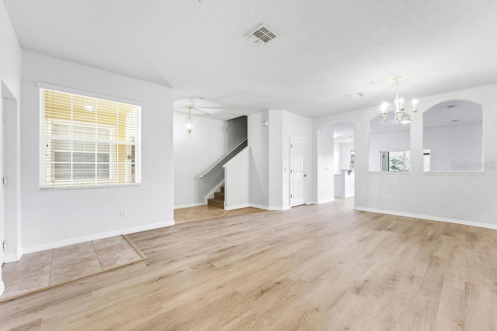 An open-concept living area features light wood-look flooring, white walls, and a staircase — 2795 OAKWATER DR, KISSIMMEE, FL