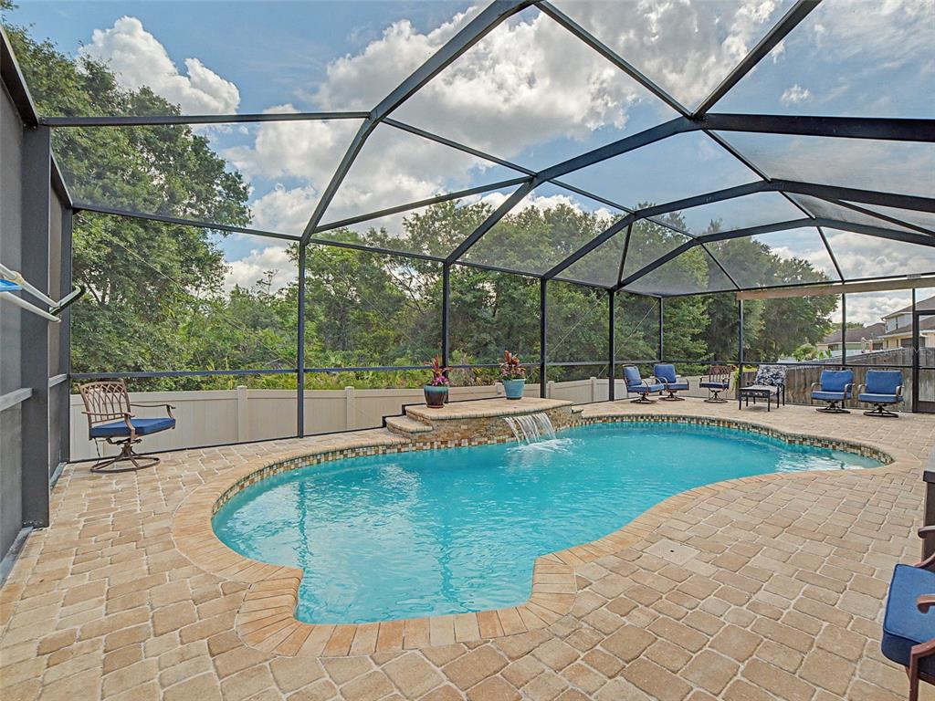 A screened-in pool area features a stone-tiled deck, a waterfall feature, and patio furniture — 11005 ROCKLEDGE VIEW DRIVE, RIVERVIEW, FL