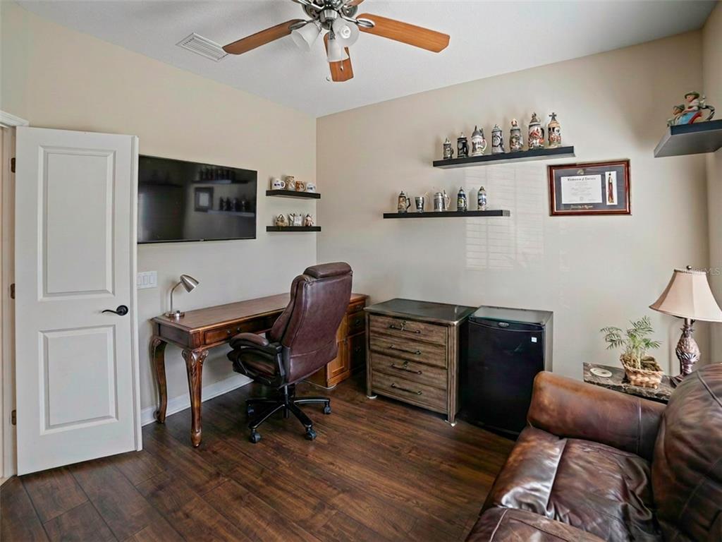 A home office features a wooden desk, leather chair, shelving with collectibles, and dark flooring — 11005 ROCKLEDGE VIEW DRIVE, RIVERVIEW, FL