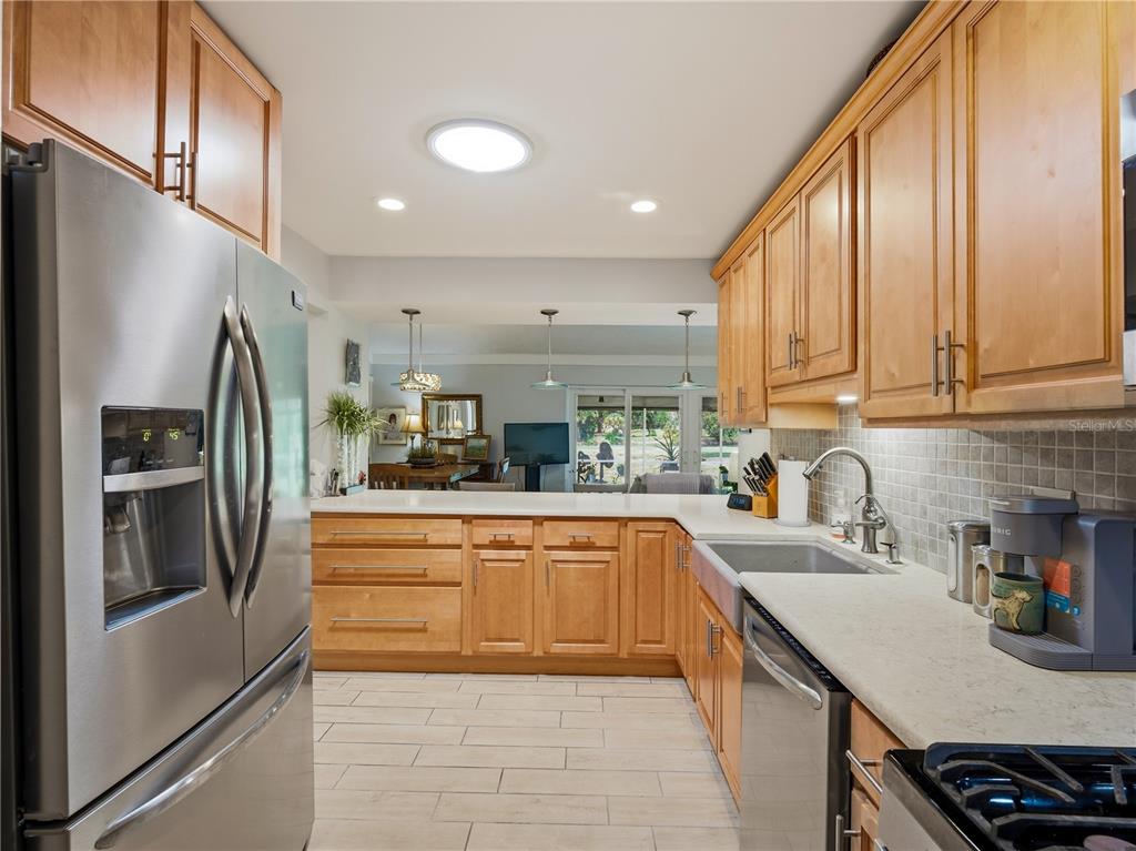 A kitchen with light wood cabinets, stainless steel appliances, and a view into the living area — 218 CANTERBURY CIRCLE, NEW SMYRNA BEACH, FL