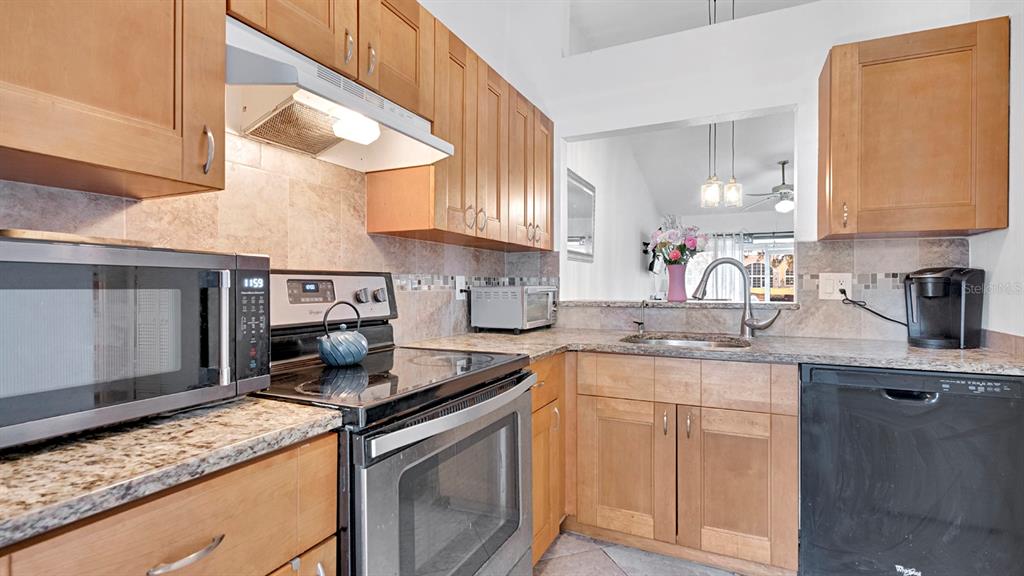 A kitchen features light wood cabinets, granite countertops, stainless steel appliances, and a pass-through window — 12 PINE ISLAND CIRCLE, KISSIMMEE, FL