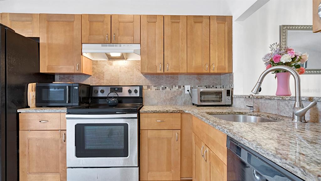A kitchen features light wood cabinets, granite countertops, stainless steel appliances, and a tile backsplash — 12 PINE ISLAND CIRCLE, KISSIMMEE, FL