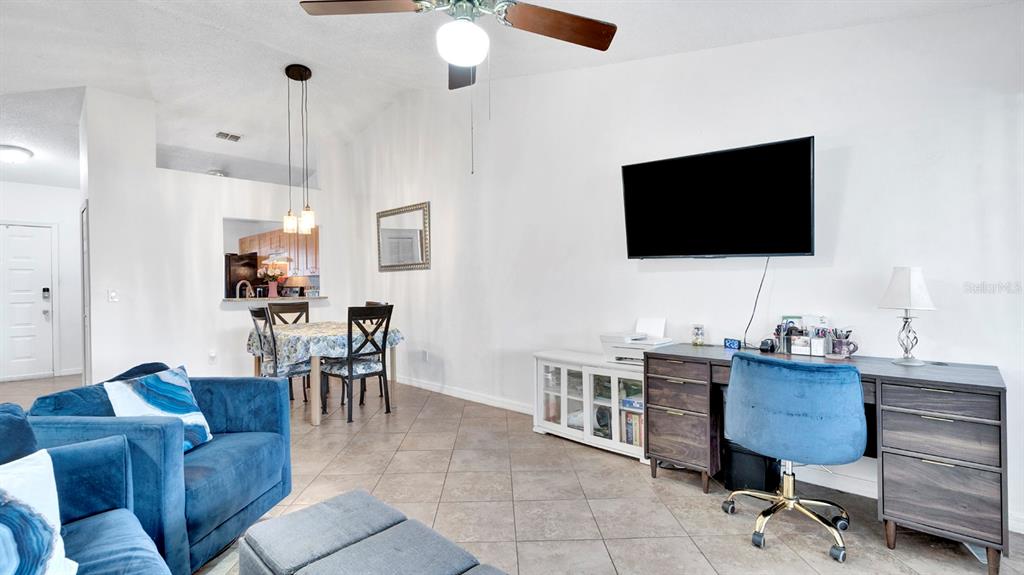 A living room features a blue sofa, a dining area, and a desk under a television — 12 PINE ISLAND CIRCLE, KISSIMMEE, FL
