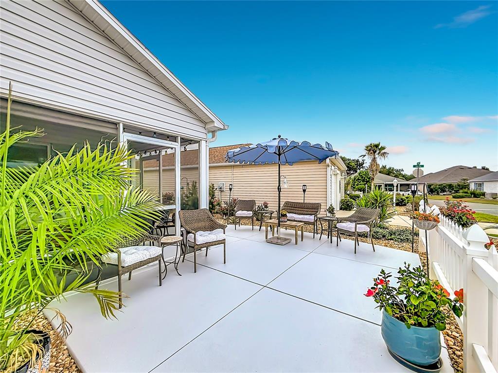 A patio with wicker furniture, a blue umbrella, and a white fence under a clear sky — 1648 ABASCO COURT, THE VILLAGES, FL