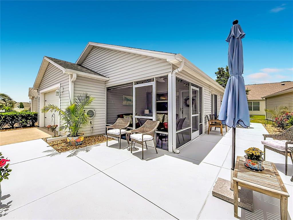 A light-colored house with a screened-in porch and a concrete patio under a blue sky — 1648 ABASCO COURT, THE VILLAGES, FL