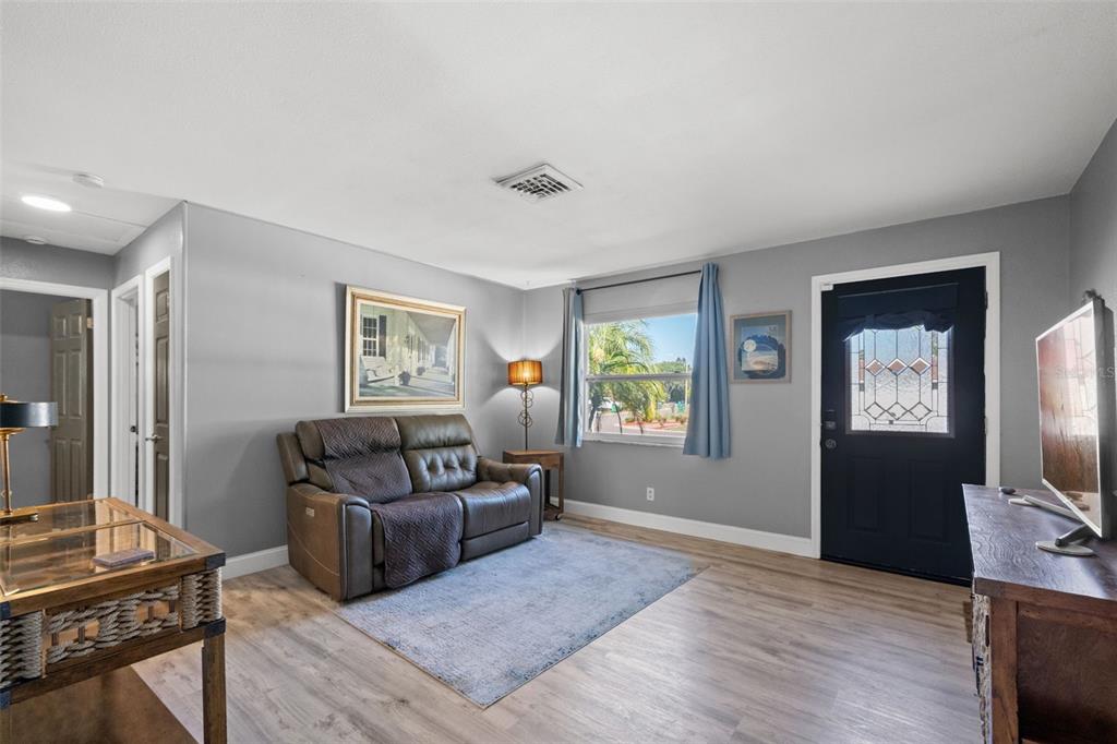 A living room features gray walls, wood-look flooring, a brown loveseat, and a black front door — 4311 63RD WAY N, ST PETERSBURG, FL