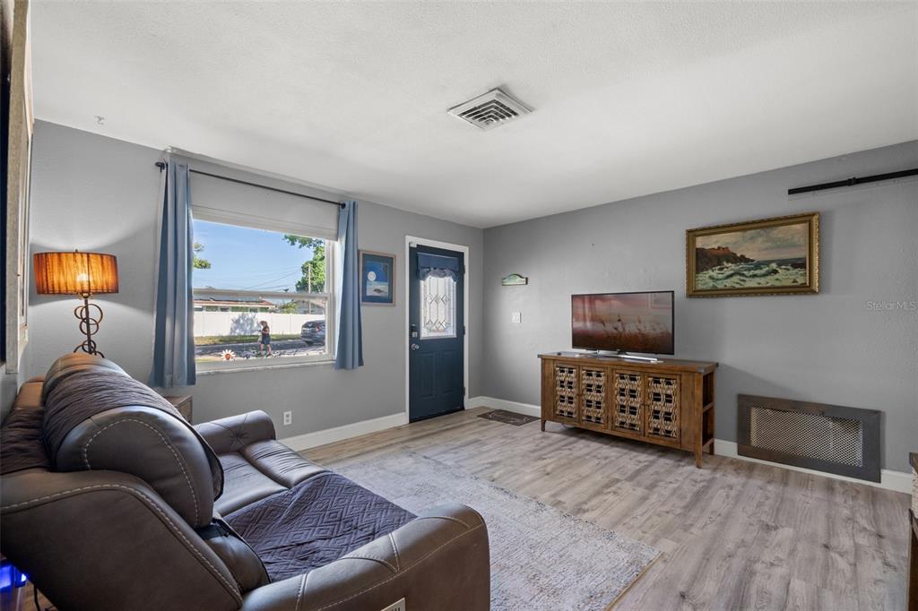 A living room features gray walls, wood-look flooring, a brown sofa, and a television console — 4311 63RD WAY N, ST PETERSBURG, FL