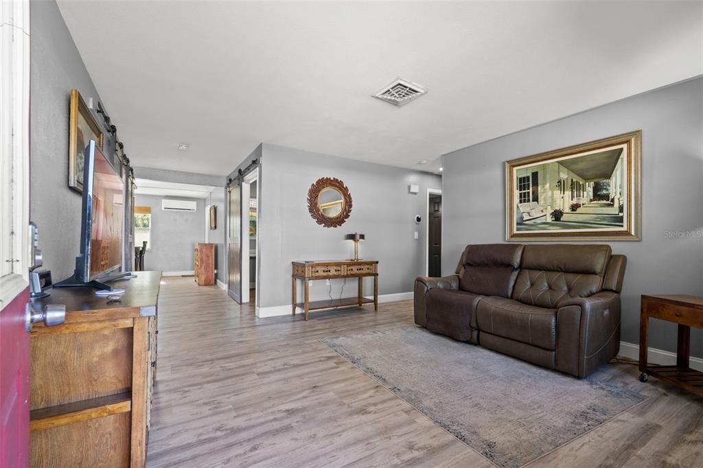A living room features gray walls, wood-look flooring, a brown leather sofa, and sliding barn doors — 4311 63RD WAY N, ST PETERSBURG, FL