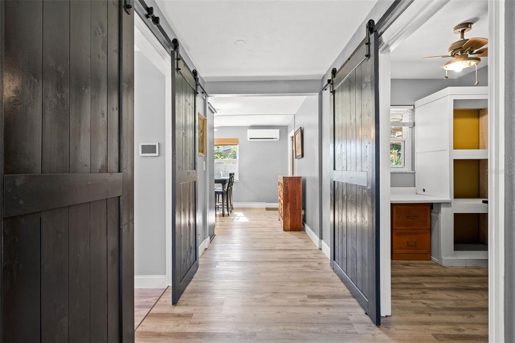 A hallway with light wood flooring features two dark sliding barn doors opening to adjacent rooms — 4311 63RD WAY N, ST PETERSBURG, FL