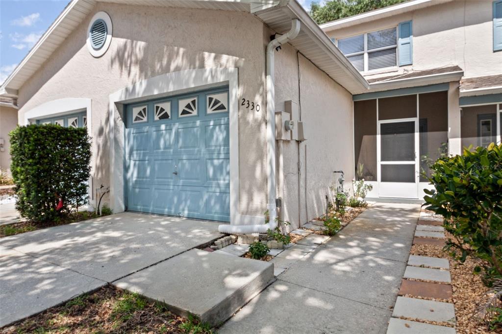 A beige house exterior with a blue garage door, a screened entryway, and concrete walkway — 2330 SE ROYAL ISLE, WINTER HAVEN, FL