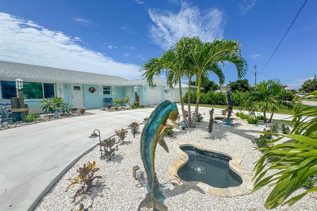 A light blue house features a concrete driveway, a small pond, and fish-shaped fountain sculptures — 1945 MICHIGAN AVENUE, ENGLEWOOD, FL