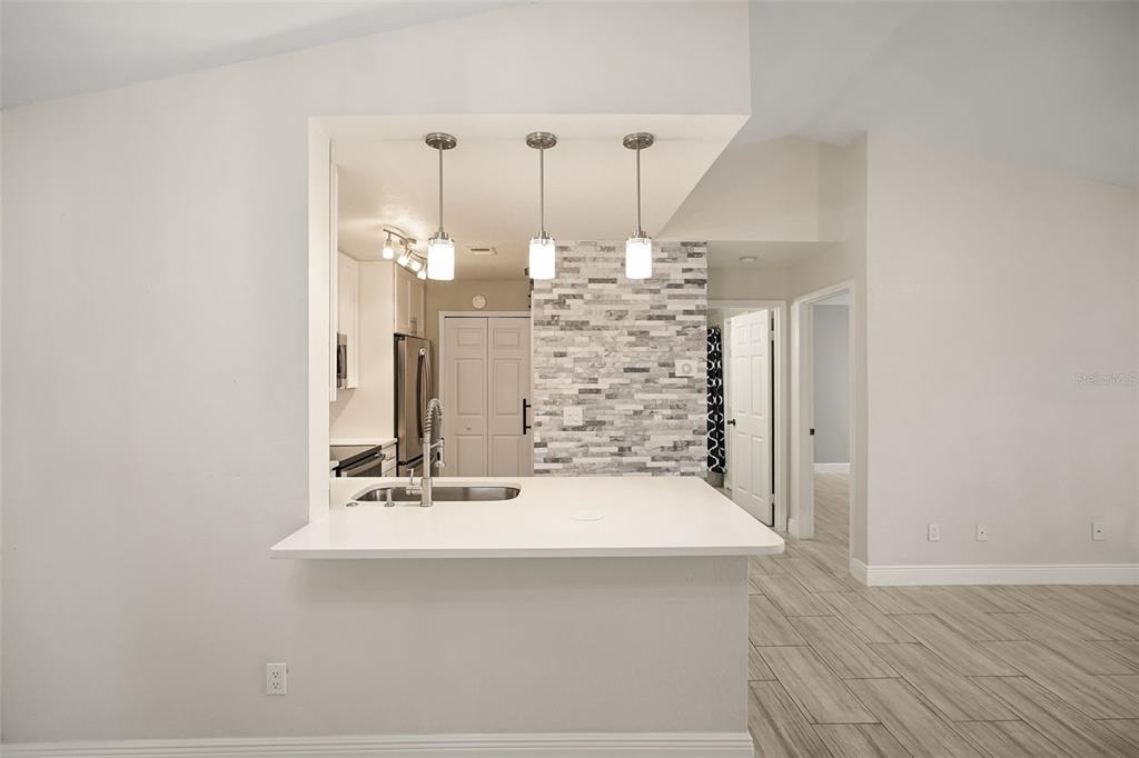 A kitchen with a breakfast bar, pendant lighting, and a stone-tiled accent wall — 7511 SEURAT STREET UNIT 10302, ORLANDO, FL