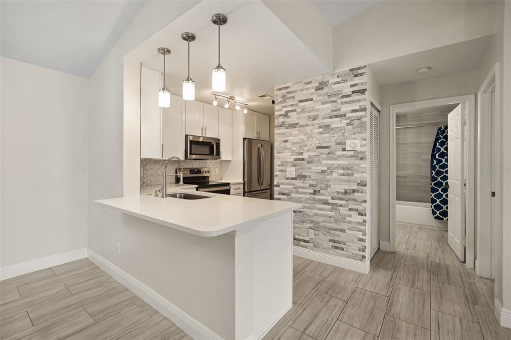 A kitchen features white cabinets, a stone accent wall, and a breakfast bar with pendants — 7511 SEURAT STREET UNIT 10302, ORLANDO, FL