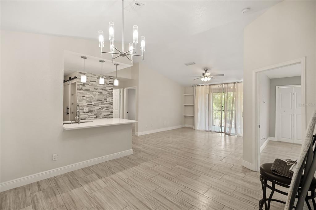 An open-concept living area features light wood-look tile flooring, a breakfast bar, and vaulted ceilings — 7511 SEURAT STREET UNIT 10302, ORLANDO, FL