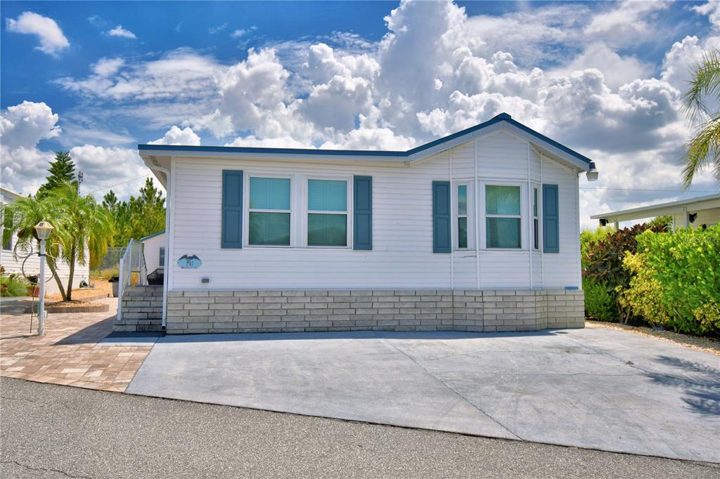 A white manufactured home with blue shutters and a concrete driveway under a cloudy sky — 251 PATTERSON ROAD UNIT I47, HAINES CITY, FL