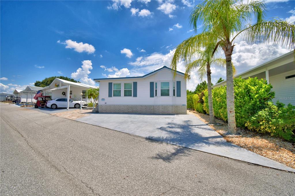 A white manufactured home with a concrete driveway and palm trees under a blue sky — 251 PATTERSON ROAD UNIT I47, HAINES CITY, FL