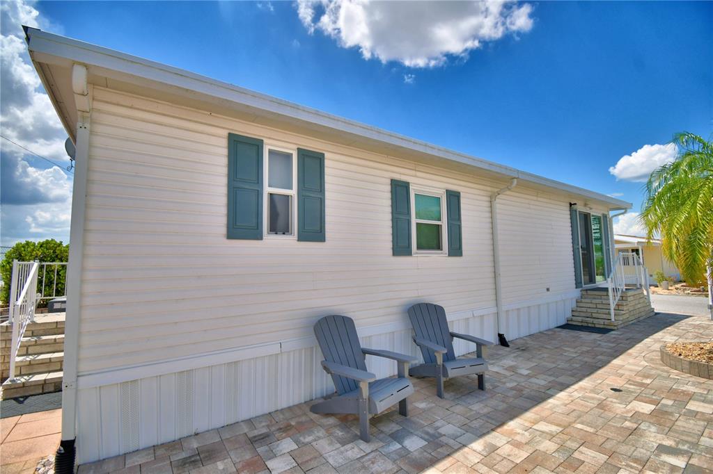 The exterior of a mobile home features white siding, blue shutters, and a paved patio area — 251 PATTERSON ROAD UNIT I47, HAINES CITY, FL