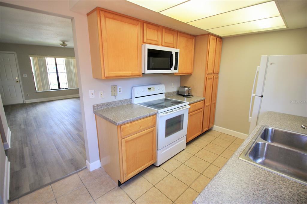 A kitchen with light wood cabinets, white appliances, and tan tile flooring — 7446 WYNNEWOOD SQUARE UNIT 190, WINTER PARK, FL