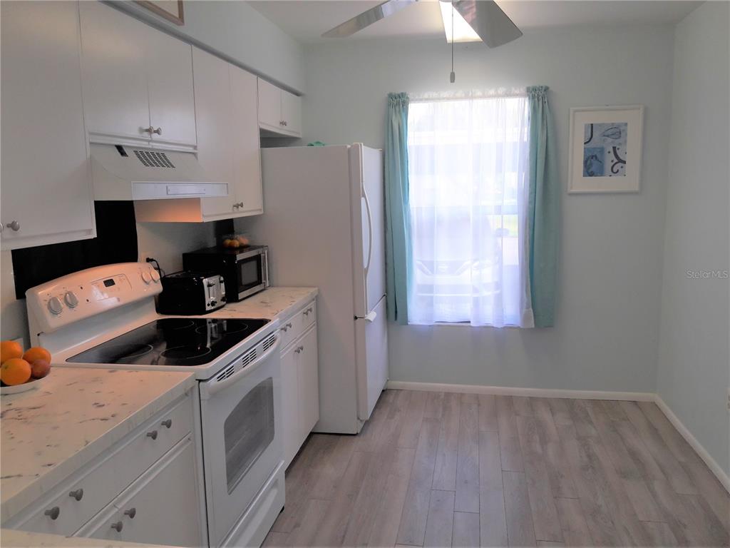 A kitchen features white cabinets, white appliances, light-colored wood-look flooring, and a window with curtains — 2713 60TH AVENUE DRIVE W, BRADENTON, FL