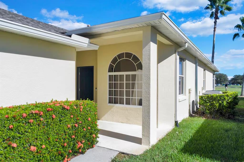 A covered entryway features a large arched window and a dark door beside a hedge — 191 CLUB VILLAS LANE, KISSIMMEE, FL