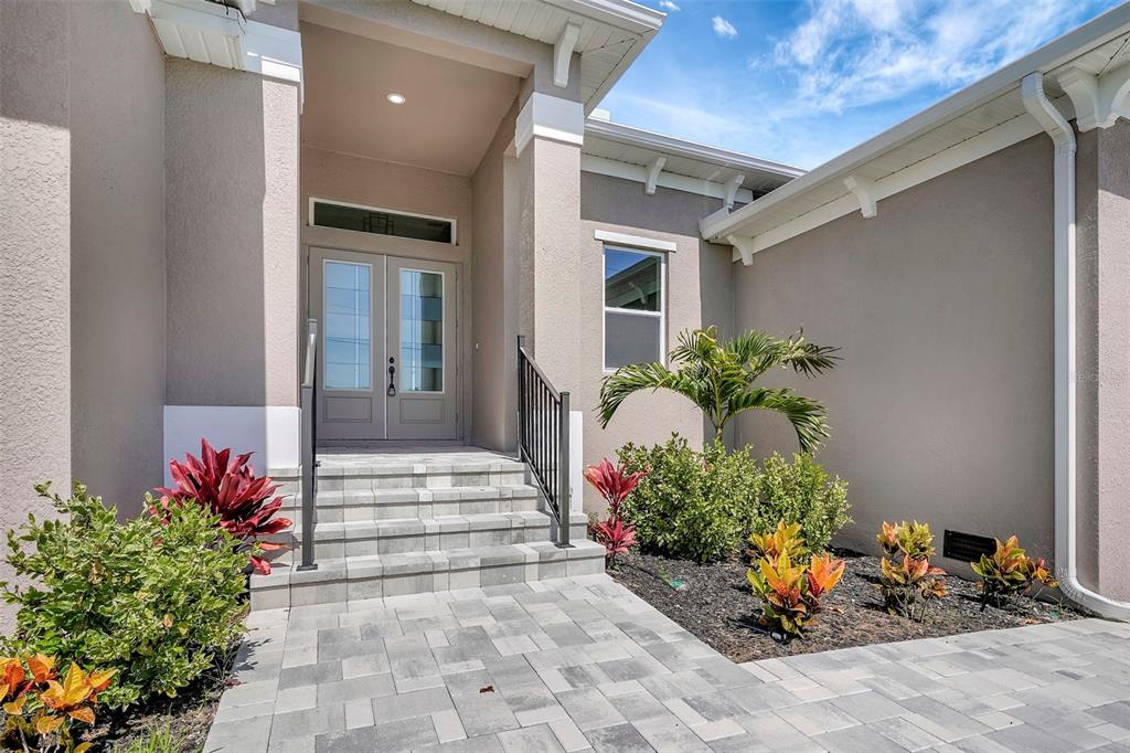 A paved walkway leads to the front entrance of a house with double glass doors — 10812 MCALESTER CIRCLE, PORT CHARLOTTE, FL