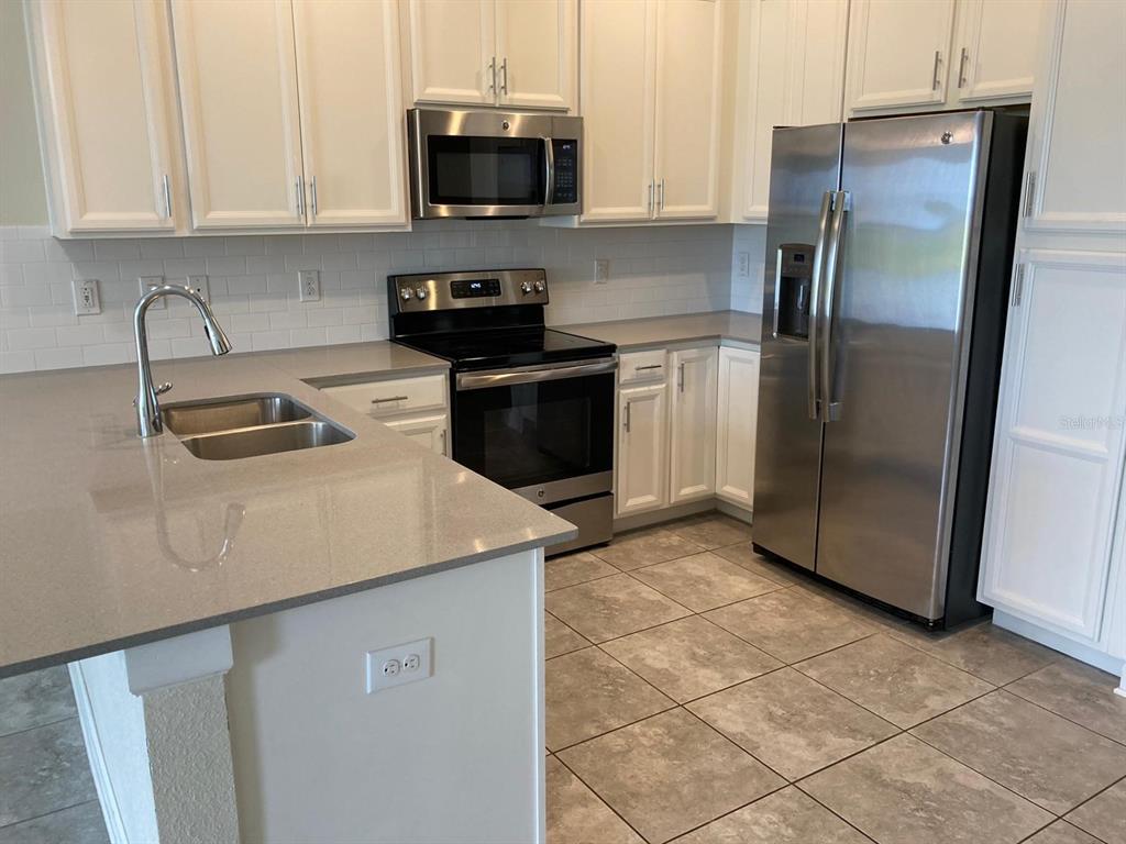 A kitchen features white cabinets, stainless steel appliances, a gray island countertop, and tile flooring — 1348 ROYAL ST GEORGE BOULEVARD, DAVENPORT, FL