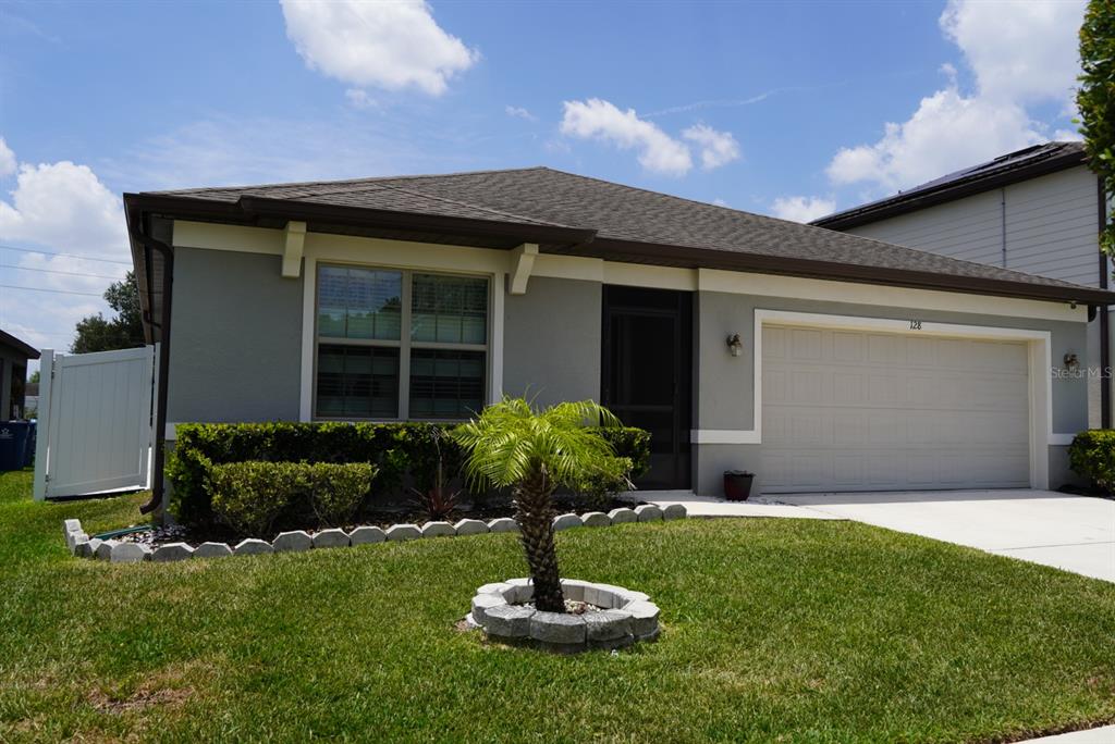 A single-story house with a gray exterior, a two-car garage, and a small palm tree — 128 CITRUS ISLE STREET S, DAVENPORT, FL