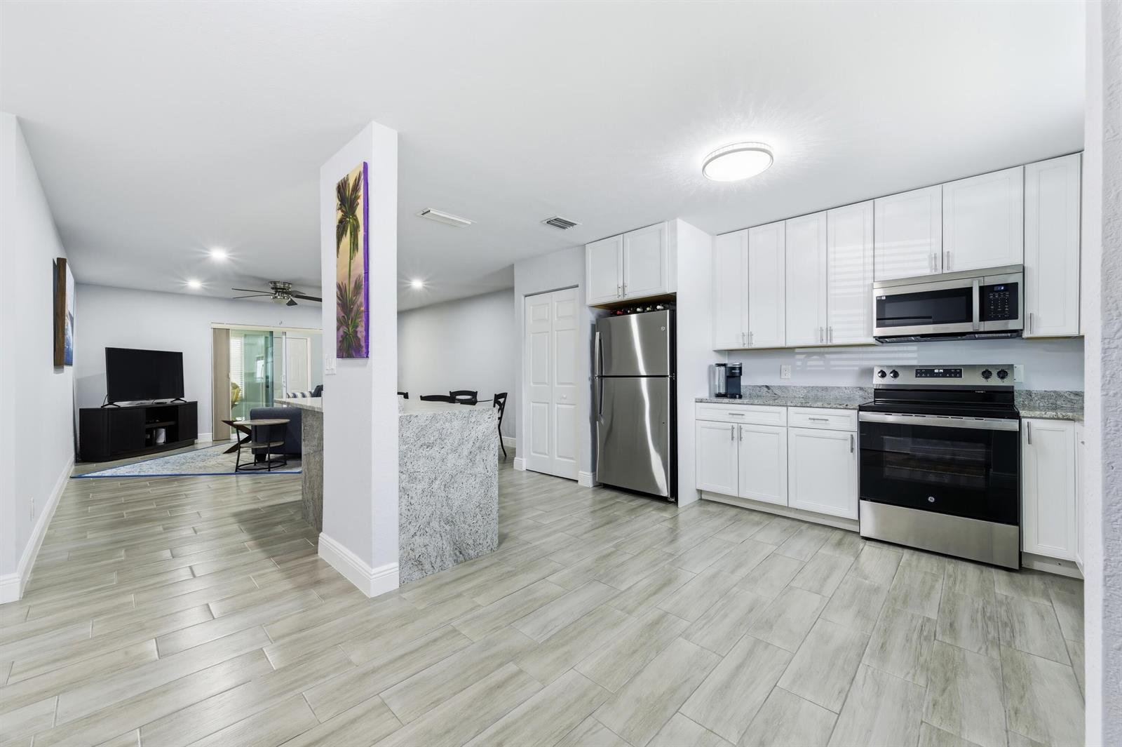 A kitchen with white cabinets, stainless steel appliances, and granite countertops opens to a living area — 586 Laconia Circle, Lake Worth FL 33467, LAKE WORTH, FL