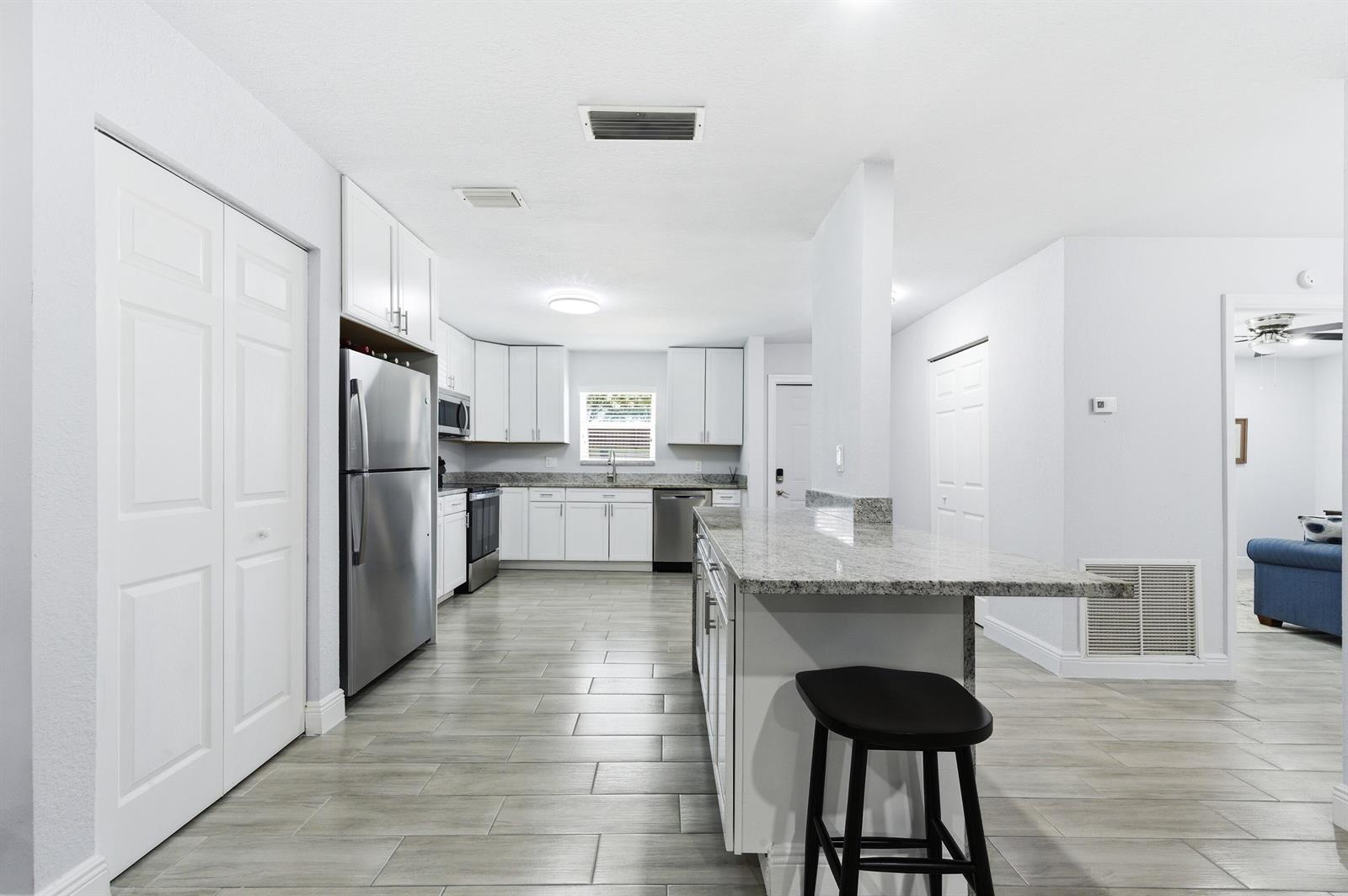 A modern kitchen features white cabinetry, stainless steel appliances, granite countertops, and light tile flooring — 586 Laconia Circle, Lake Worth FL 33467, LAKE WORTH, FL