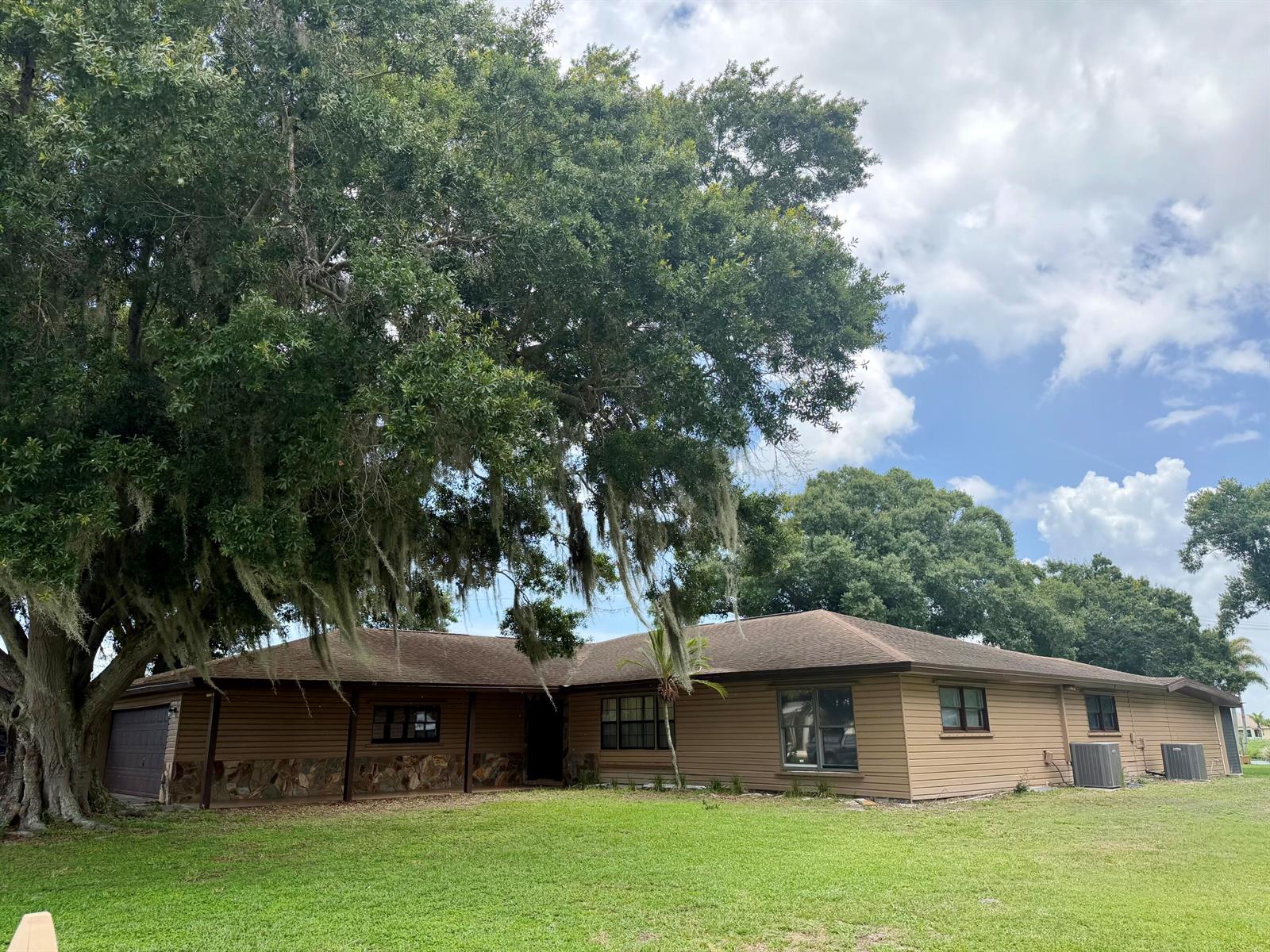 A single-story house with brown siding, a stone base, and a large oak tree — 1631 SE 24th Boulevard, Okeechobee FL 34974, OKEECHOBEE, FL