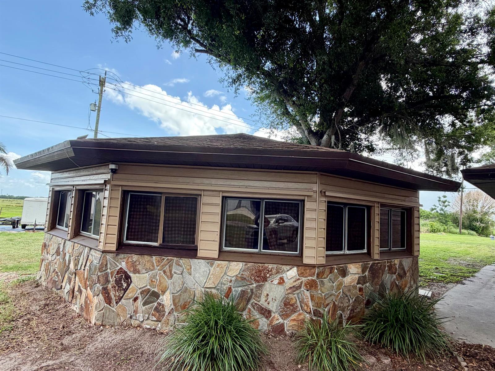 A single-story building with a stone base, horizontal siding, and multiple windows under a tree — 1631 SE 24th Boulevard, Okeechobee FL 34974, OKEECHOBEE, FL