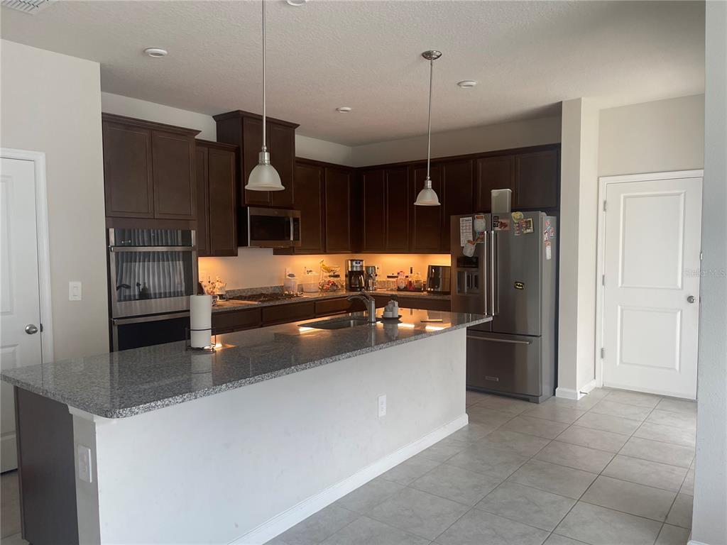 A kitchen features dark wood cabinets, granite countertops, stainless steel appliances, and a central island — 3954 GREAT SMOKEY WAY, APOPKA, FL