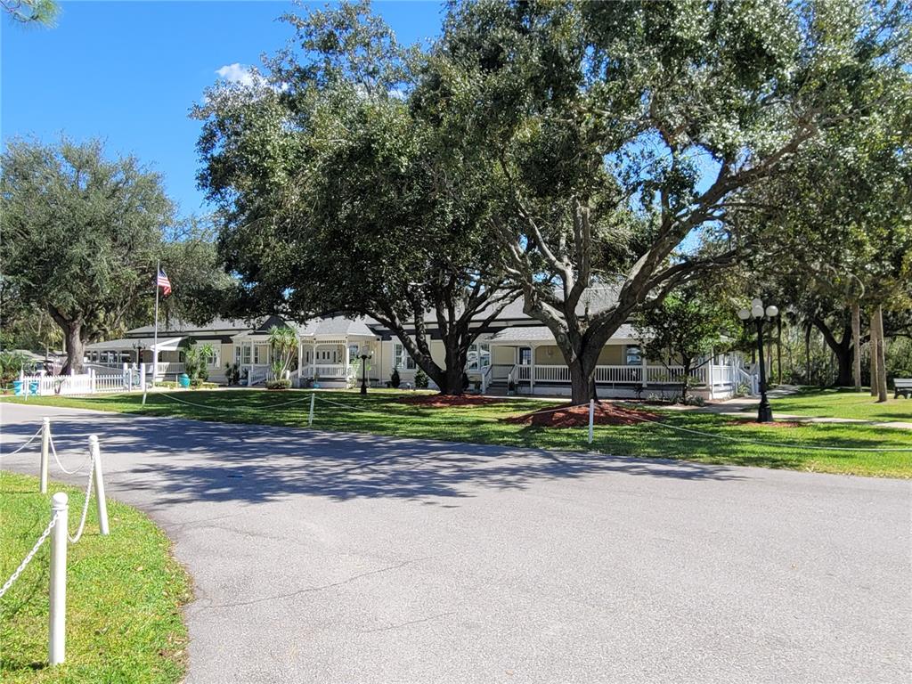 A light-colored, single-story building with a wrap-around porch sits behind large trees and lawns — 213 YORK COTTAGE DRIVE, HAINES CITY, FL