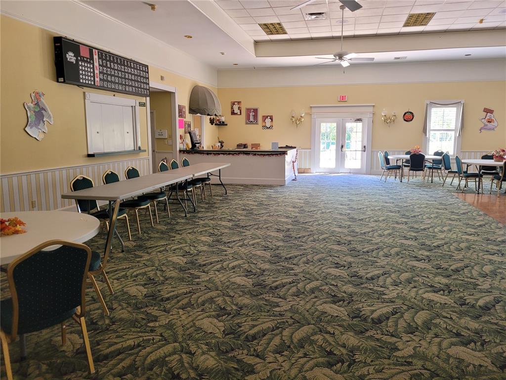 A large community room features a bingo board, long tables, chairs, and patterned carpeting — 213 YORK COTTAGE DRIVE, HAINES CITY, FL