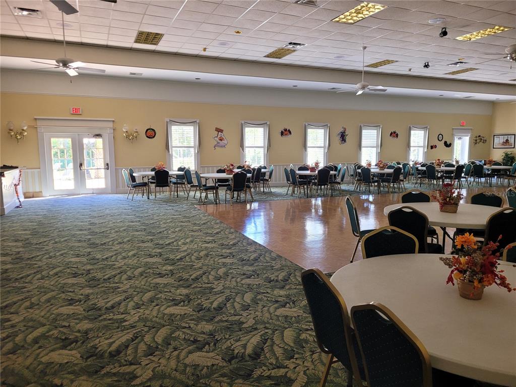 A large community hall features a patterned carpet, a wooden dance floor, and round tables — 213 YORK COTTAGE DRIVE, HAINES CITY, FL
