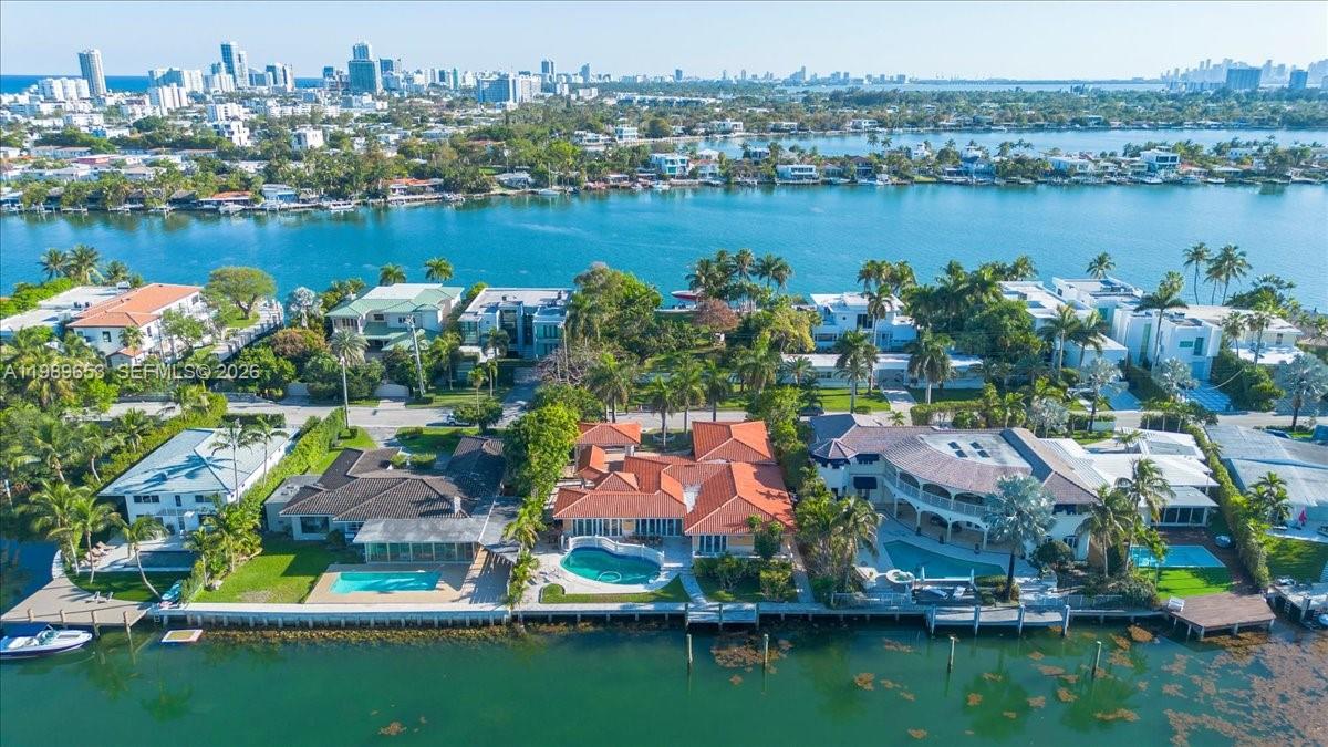 An aerial view shows waterfront houses with pools along a canal near a city skyline — 1249 Biscaya Dr, Surfside FL 33154, SURFSIDE, FL