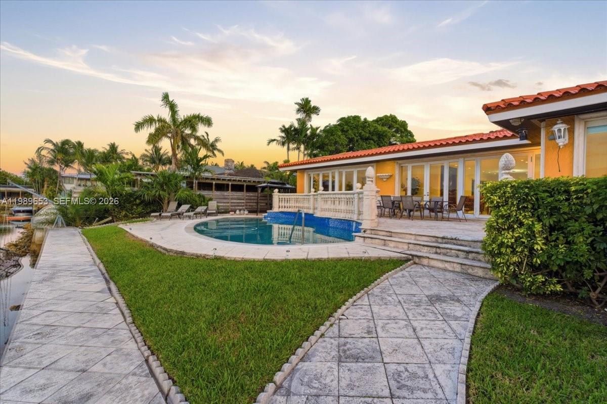 A backyard features a swimming pool, stone patio, and lawn next to a waterfront house — 1249 Biscaya Dr, Surfside FL 33154, SURFSIDE, FL