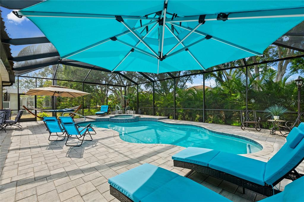 A screened-in pool area features a large blue umbrella, lounge chairs, and a hot tub — 9211 12TH AVENUE NW, BRADENTON, FL