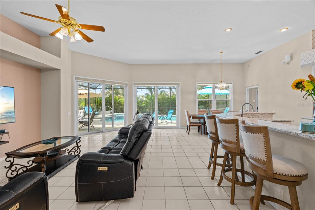 An open-concept living room and kitchen featuring tile floors, leather furniture, and sliding glass doors — 9211 12TH AVENUE NW, BRADENTON, FL